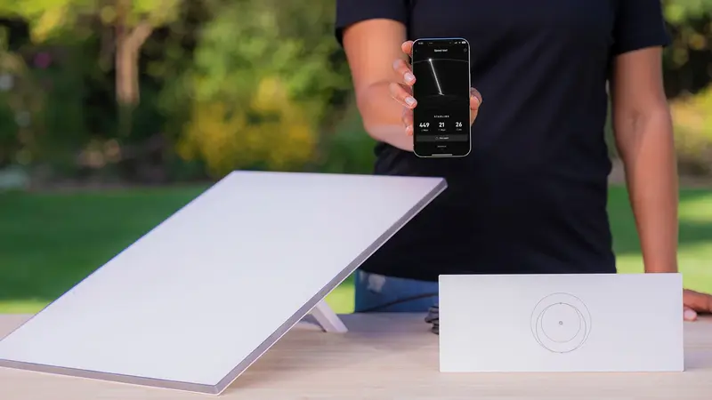 Starlink anténa, router a mobilná aplikácia na stole v záhrade